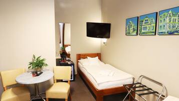 Habitación de hotel con cama, televisor montado en la pared, una mesita redonda con sillas y una planta.