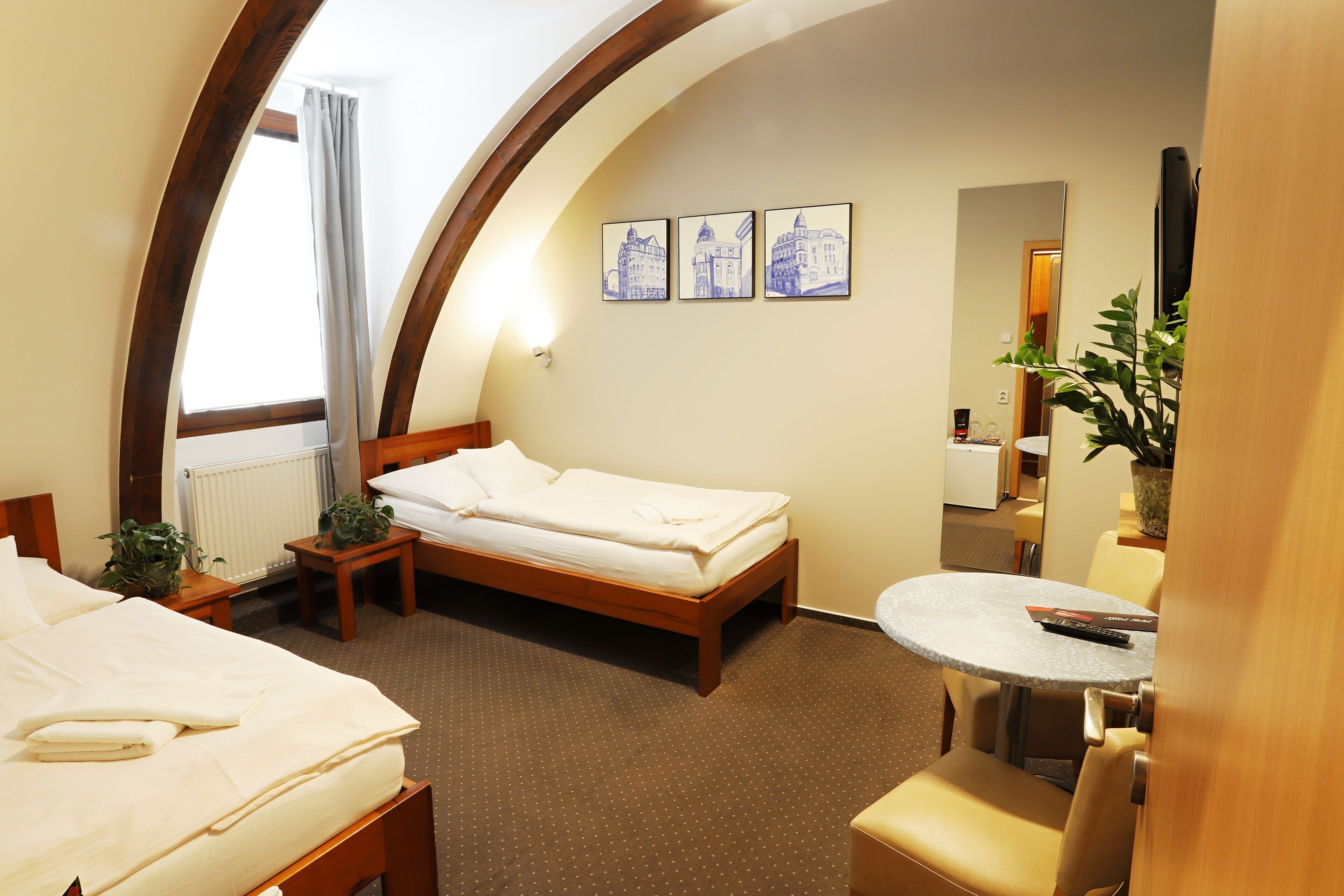 A hotel room with a bed, a small table, a chair, a potted plant, and a mirror.
