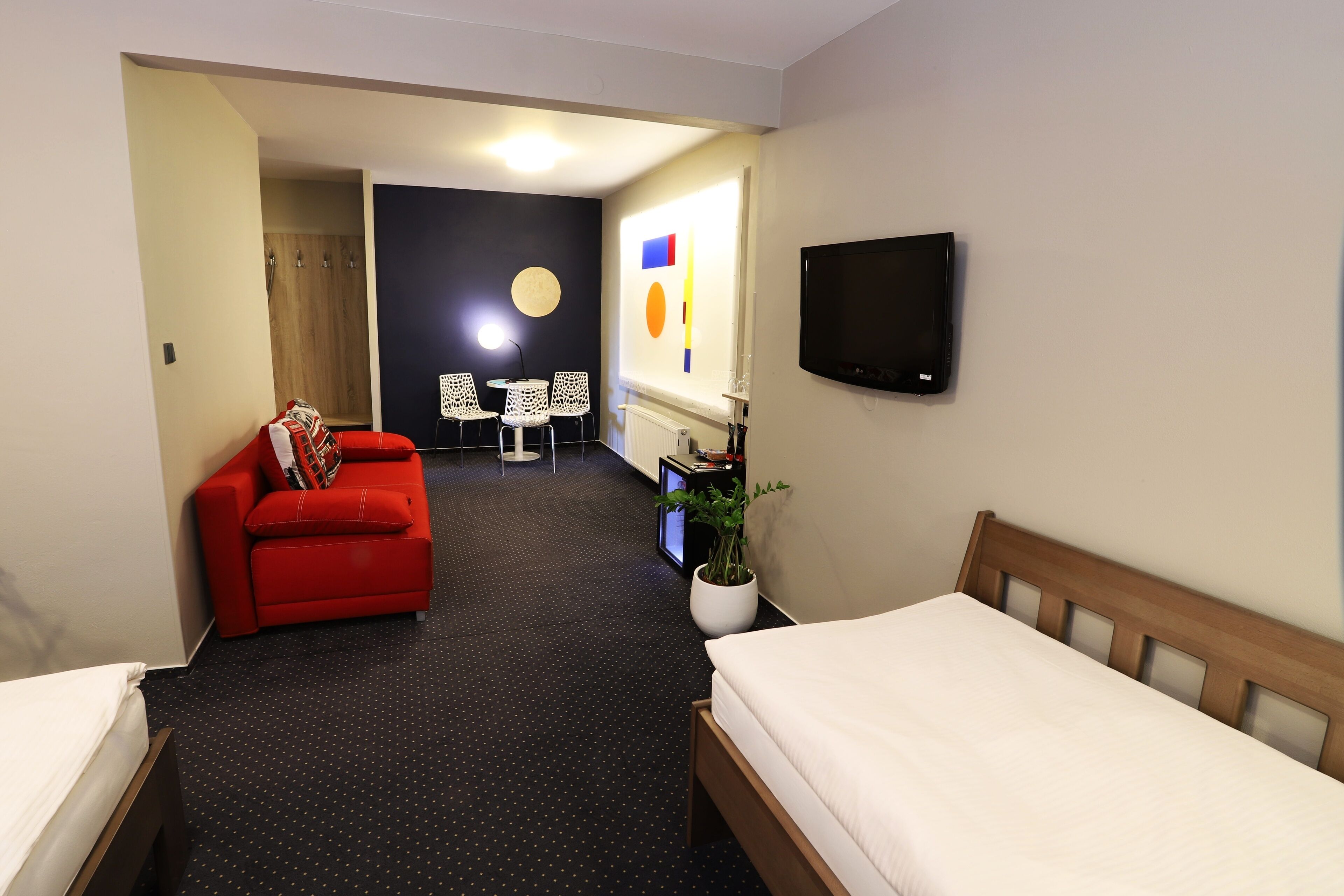 Et hotelværelse med en seng, en rød sofa, et fjernsyn, en plante og et lille bord med stole.