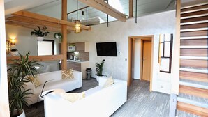 Un espacio de sala moderno con un sofá, plantas en macetas y una cocina al fondo.