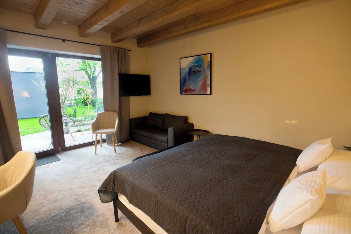 Una camera da letto con un letto grande, un divano, una poltrona, una TV e una porta scorrevole in vetro che dà su un balcone.