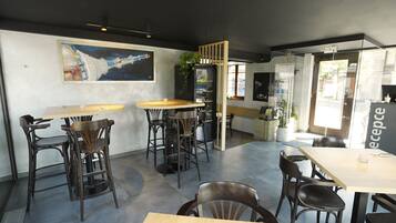 Un restaurante moderno con mesas y sillas altas, un cuadro grande en la pared y un separador de vidrio.