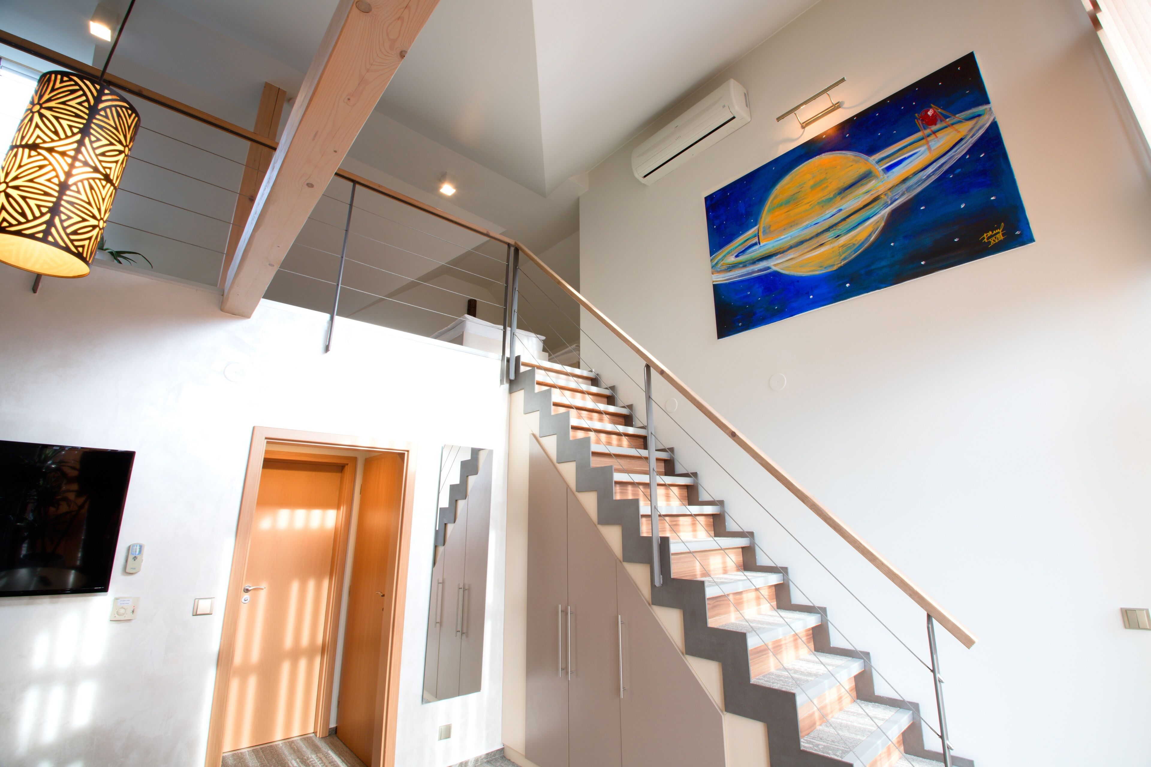 Una escalera de diseño moderno, un cuadro de un planeta en la pared y una lámpara colgante.