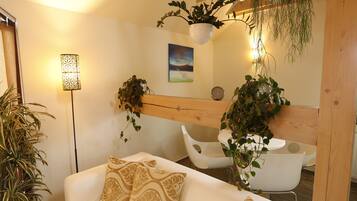 A modern living room with a white sofa, patterned cushions, a hanging plant, and a white chair.