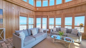 A spacious living area with a large window overlooking the beach, furnished with two sofas and a coffee table. - Boat House- Oceanfront Hot Tub! Creekfront, Dock & Pool (Pawleys Island)