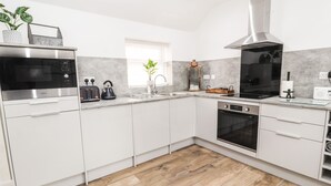 Une cuisine moderne avec des armoires blanches, une hotte de cuisinière en acier inoxydable, un four à micro-ondes, un grille-pain et une bouilloire.
