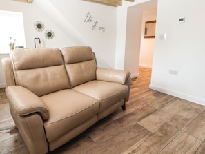 A tan leather sofa in a room with wooden flooring, white walls, and decorative hexagonal wall art. - Afallon Cottage (Rhyl)