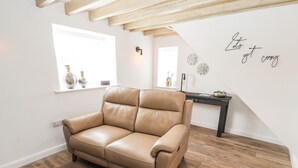 Un canapé en cuir marron dans une pièce dotée d’un plancher en bois, de murs blancs et d’un plafond en pente.