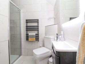 A modern bathroom with a glass shower enclosure, a white toilet, a towel rack with a towel, and a sink with toiletries. - Afallon Cottage (Rhyl)