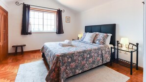Een slaapkamer met een bed, nachtkastje, raam met gordijnen, een houten deur en een kleine tafel.