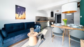 Ein modernes Wohnzimmer mit einem blauen Sofa, einem Couchtisch und einem Essbereich mit einem Holztisch, gedeckt für vier Personen.
