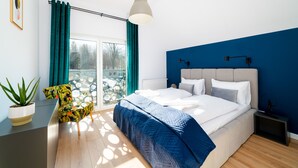 Ein modernes Schlafzimmer mit einem großen Bett, einer Topfpflanze und Blick ins Freie.