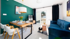Ein modernes Wohnzimmer mit einem blauen Sofa, einem Holzespeisetisch gedeckt mit Tellern und Gläsern, einem Fernseher und einer Vase mit Tulpen.