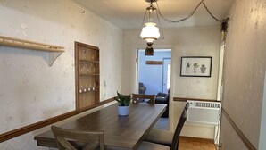 A dining area with a wooden table, chairs, a potted plant, a chandelier, and a wall-mounted shelf with glassware. - Hidden gem, 2BR-2 Living, quiet neighborhood (Plattsburgh)