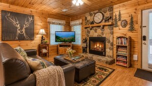 A cozy log cabin interior with a fireplace, television, leather furniture, and a bookshelf.