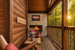 A log cabin with a stone fireplace, wooden deck, and a sign that reads 'Sit Long Talk Much.'