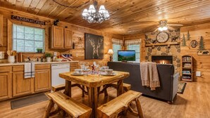 A cabin interior with a wooden dining table, benches, a fireplace, a television, and a kitchen area. - American Spirit, Free Tickets, Hot Tub, WIFI, “Cozy Cabin Retreat in the Smokies (Sevierville)