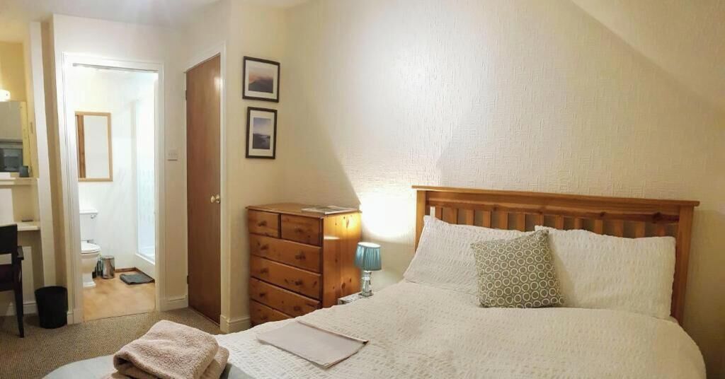 A bedroom with a bed, a dresser, a lamp, and a door leading to a bathroom.