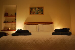 Quarto de hotel com uma cama, um quadro na parede e uma estante com objetos.