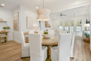 A spacious dining area with a round table, white chairs, and a hanging light fixture.