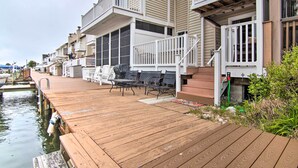 Eine Holzterrasse mit Gartenmöbeln, ein Steg, der sich über das Wasser erstreckt, und ein Gebäude mit Balkonen.