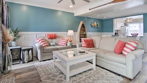 Ein Wohnzimmer mit Deckenventilator, einem Glastisch, zwei Sofas mit Streifenmustern sowie einem kleinen Beistelltisch und einem dekorativen Regal.
