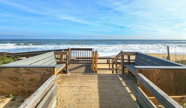 A wooden boardwalk leading to a beach with a wooden bench and a sign indicating a short distance to the beach.