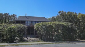 A two-story building with a balcony, surrounded by dense shrubbery. - Tara - Enjoy easy beach access from this Traditional 3 BR Beach Cottage in Southern Shores (Southern Shores)
