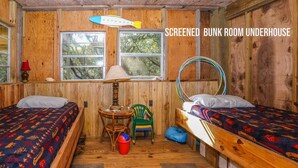 A screened bunk room underhouse with two beds, a small table, chairs, and a window with a view of trees. - Tara - Enjoy easy beach access from this Traditional 3 BR Beach Cottage in Southern Shores (Southern Shores)