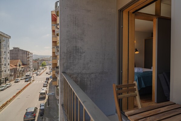 A balcony with a view of a city street, a wooden bench, and a bed with a blue blanket.