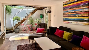 Un soggiorno moderno con un divano, poltrone rosse, un tavolo e un quadro astratto dai colori vivaci.