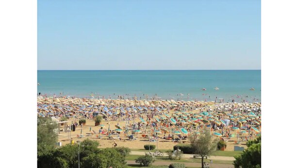 Een druk strand met veel parasols en mensen die van het zonnige weer genieten.