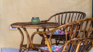 Ein Korbtisch mit einer Mosaikvase, begleitet von Korbstühlen mit Blumenkissen.