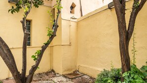 Ein schmaler Innenhof mit einer gelben Wand, einem kleinen Fenster und einem Metallaushahn.