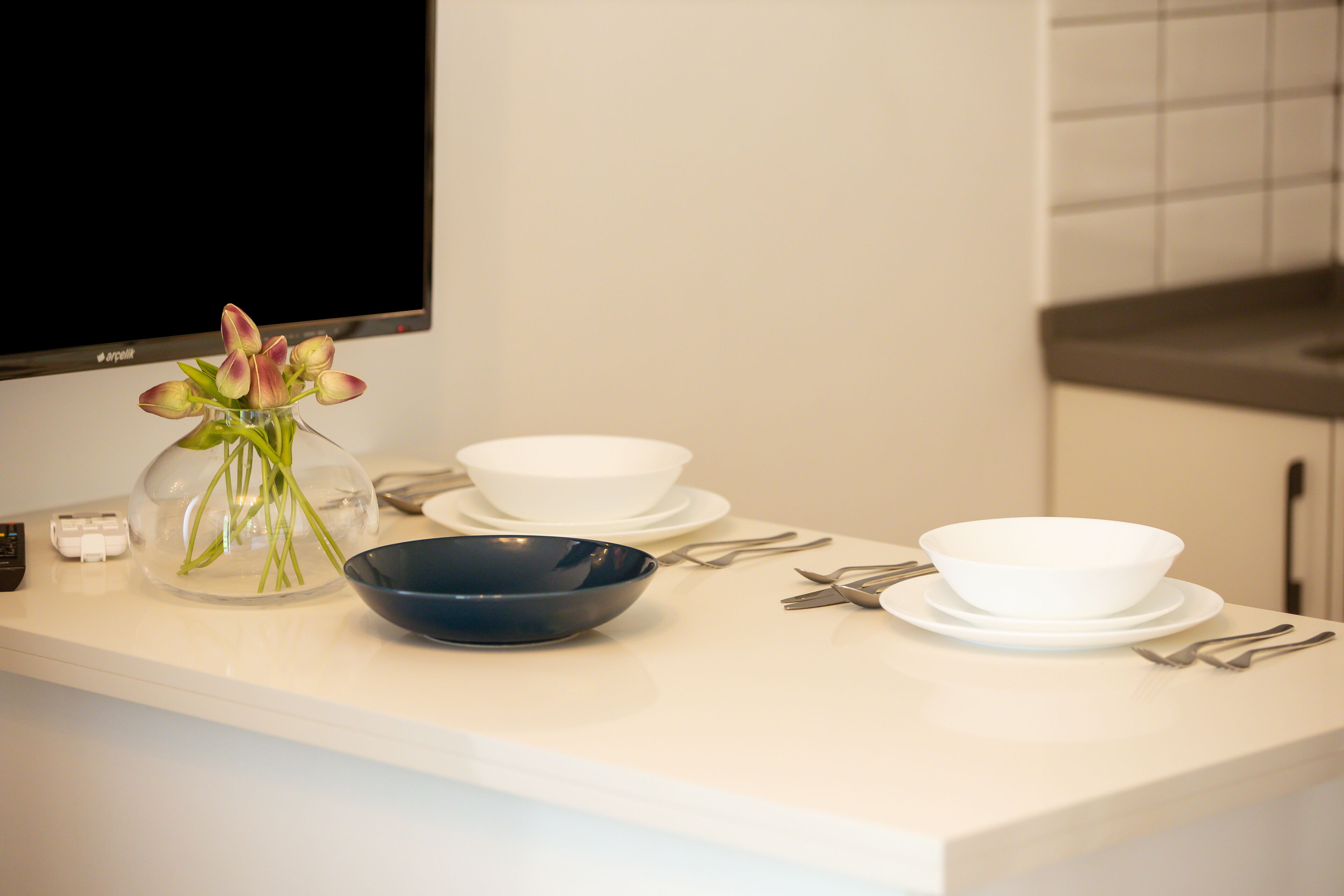 A kitchen counter with a vase of flowers, a black bowl, white bowls, and utensils.