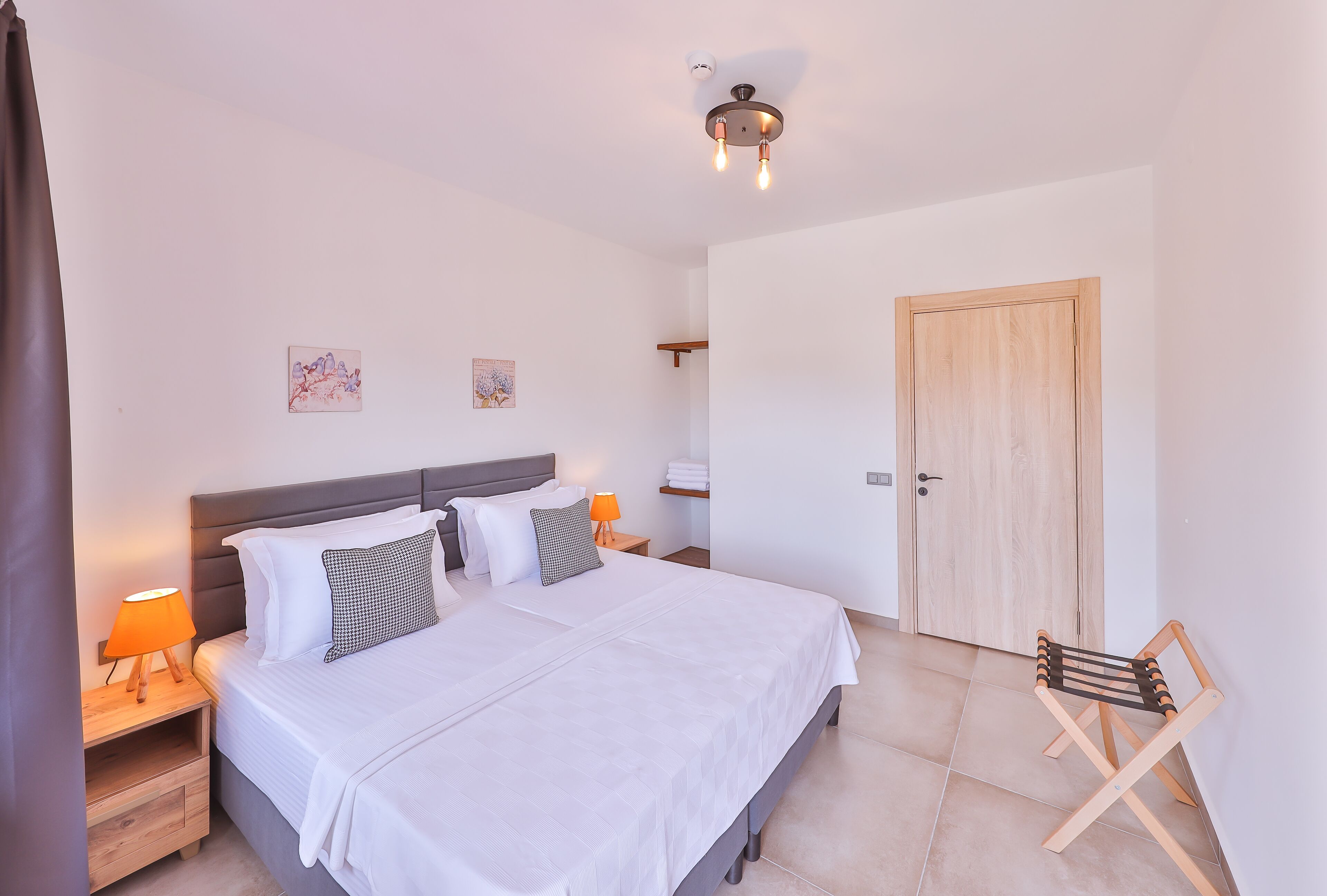 A neatly made bed with white linens, a bedside lamp, and a small wooden nightstand.