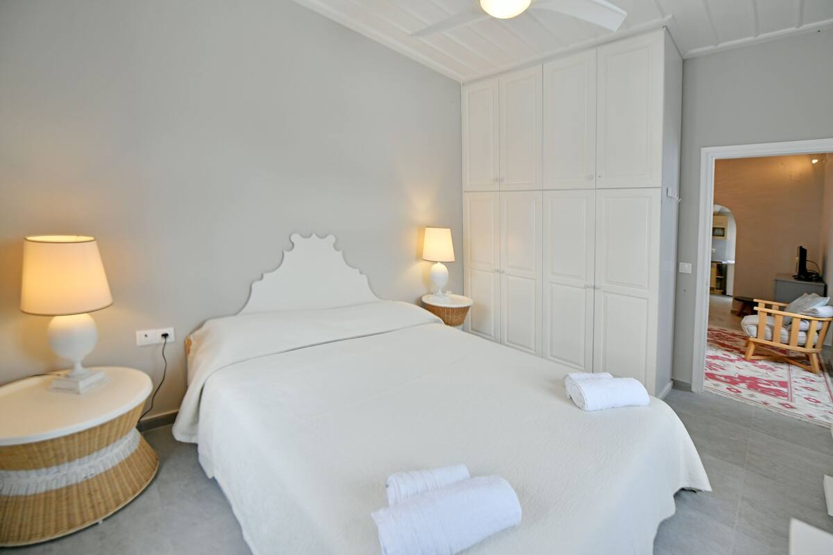 A hotel room with a large bed, two bedside lamps, a wicker side table, and a wardrobe.
