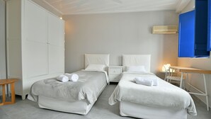 A hotel room with two beds, a desk, a chair, a wardrobe, and an air conditioning unit. - Bexis Residences Hydra (Hydra)