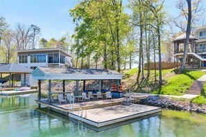 Une maison moderne avec un quai s’avançant dans un lac, entourée d’arbres et sous un ciel dégagé.