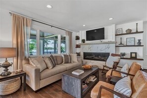 Un salon comprenant un canapé, une table basse et des fauteuils, une cheminée et un téléviseur fixé au mur.