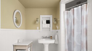 A bathroom with a white pedestal sink, a mirror, a towel rack, and a shower curtain.
