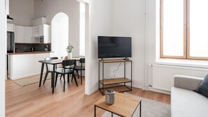 A modern living room with a TV on a stand, a sofa, and a dining area with chairs and a table. - Stylish Historical Loft with Sauna & Free Parking (Tampere)