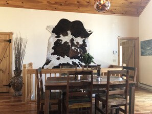 A dining area with a wooden table and chairs, a large cowhide artwork on the wall, and a wooden ceiling. - Heaven on Earth Nestled in the Blue Ridge Mountains (Vilas)