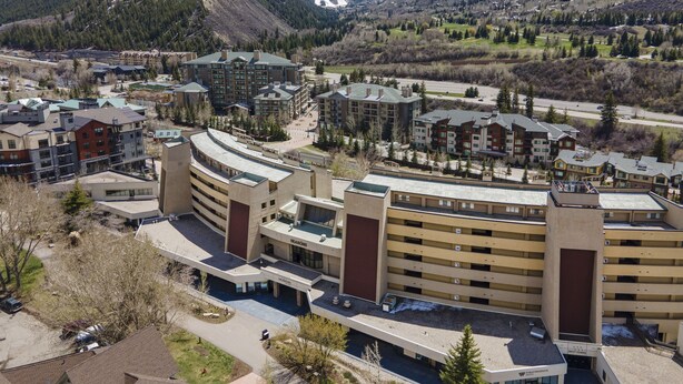 A modern hotel complex with multiple buildings, a central courtyard, and a mountainous backdrop. - Prime Avon Location | Walk to Gondola & Dining | River Trail Access & Views (Avon)