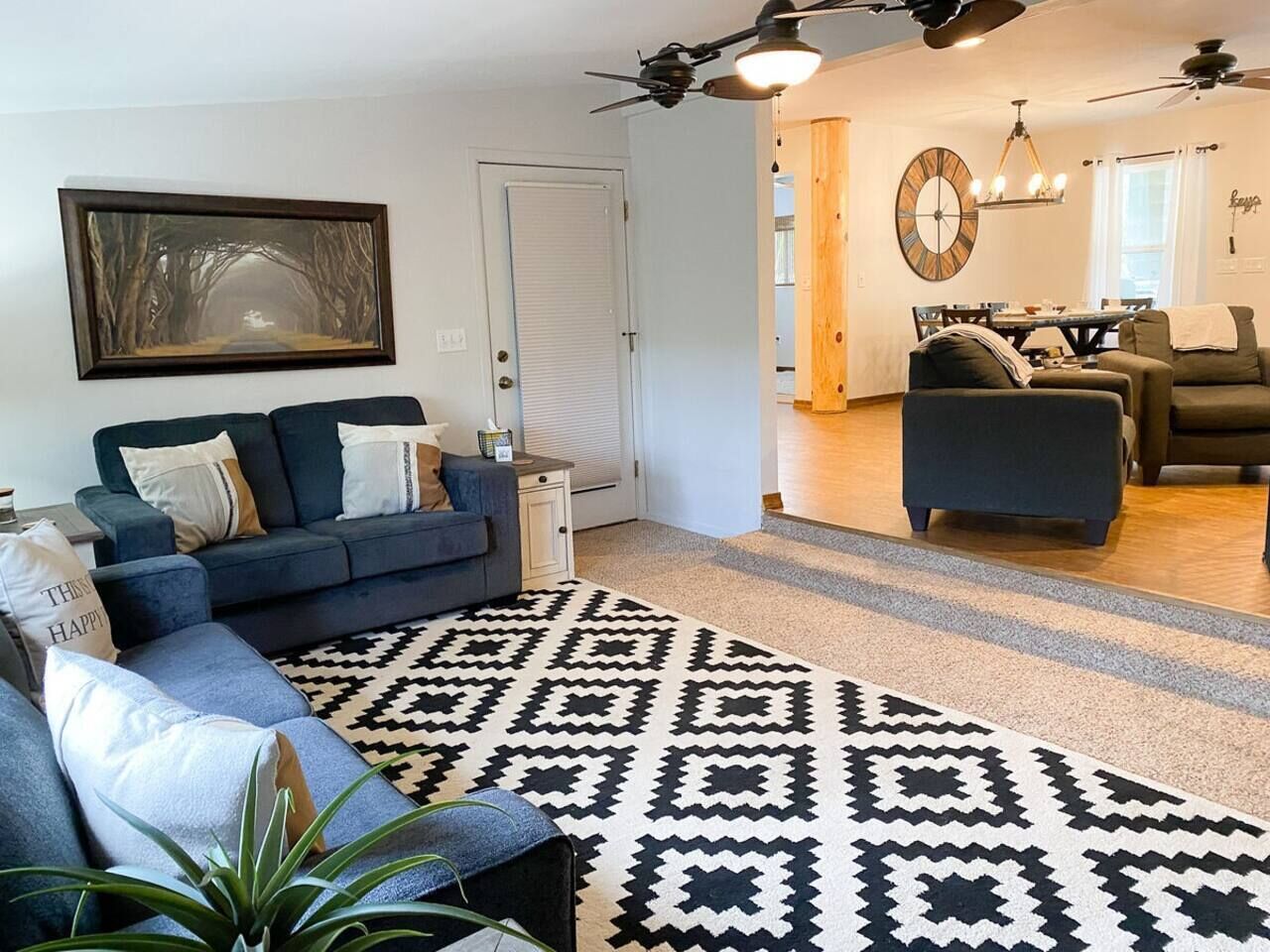 A living room with a sofa, a patterned rug, a dining area with a table and chairs, and a ceiling fan.
