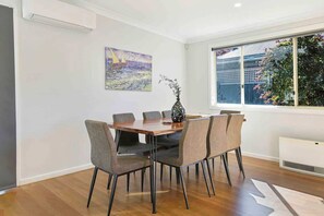 Ein Essbereich mit einem Holztisch, sechs Stühlen, einer Vase mit Zweigen und einem Bild an der Wand.