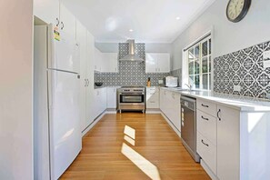 A modern kitchen with white cabinets, a stainless steel stove, and patterned backsplash tiles. - Cottage on Lords - Pet Friendly (Orange)