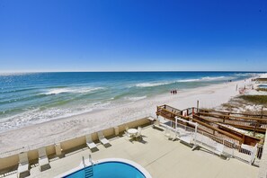 Blick auf einen Strand mit Pool, Liegestühlen und einer Holzterrasse.
