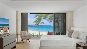 Une chambre moderne avec un grand lit, une télévision, un fauteuil et une vue sur la plage.