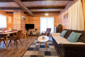 A cozy cabin interior with a dining area, a sofa, and a television. - Chalet Markoci With Hot Tub (Rakovica)